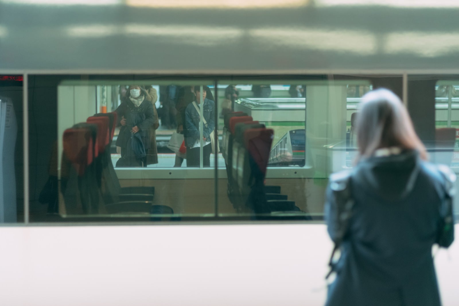 「停車中の電車越しに見る利用客」の写真