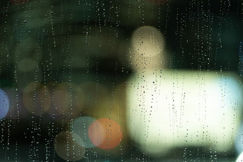 雨の窓ガラス越しに見えるネオンの写真