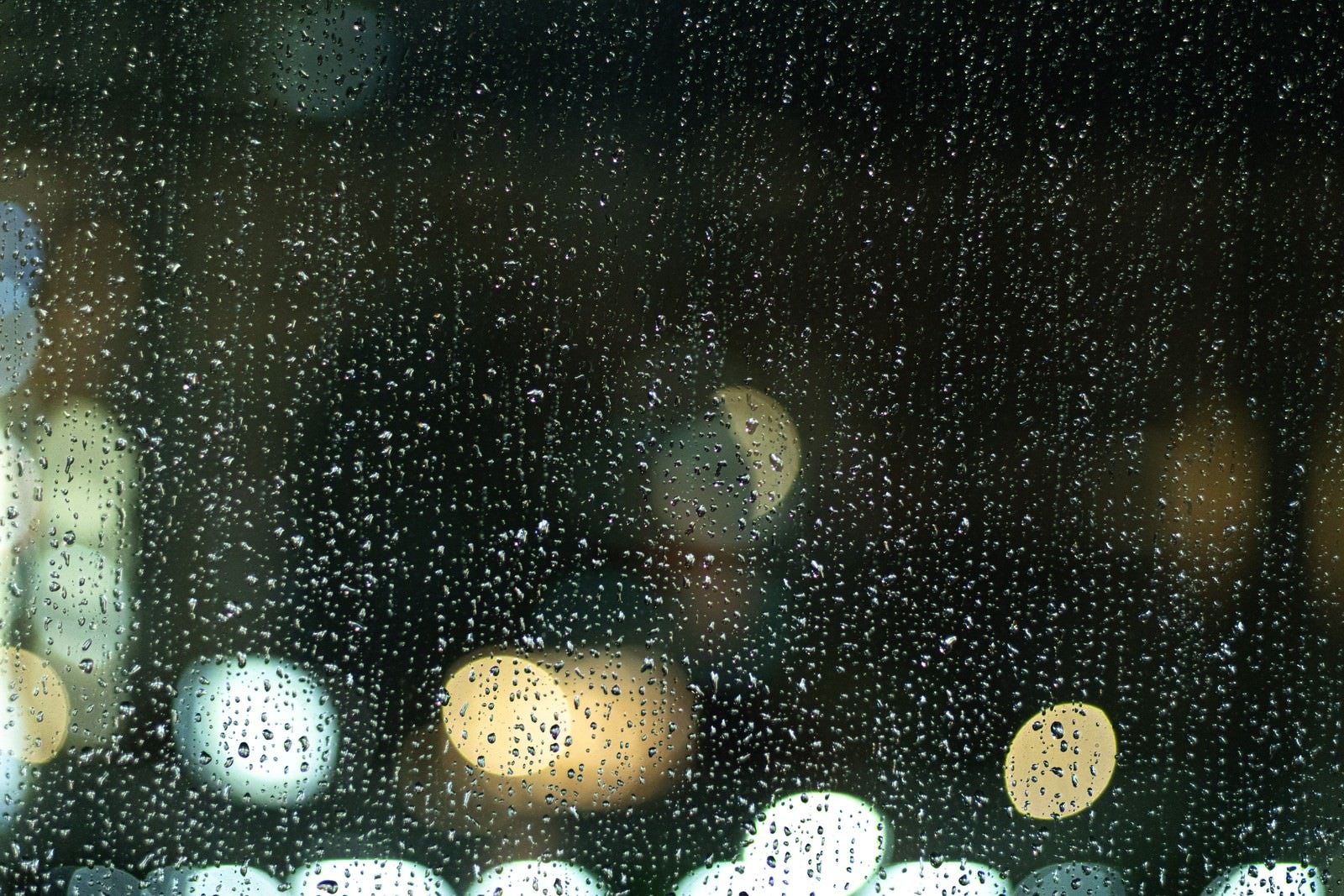 「窓ガラス一面に残る雨粒と街の明かり」の写真