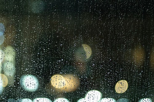 窓ガラス一面に残る雨粒と街の明かりの写真