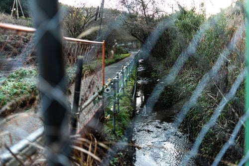 フェンス越しに見た側溝を流れる水の写真