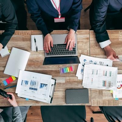 紙の資料とパソコンを用いてディスカッションする会議の写真