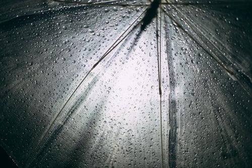 雨が強く降る夜のビニール傘と街灯の写真