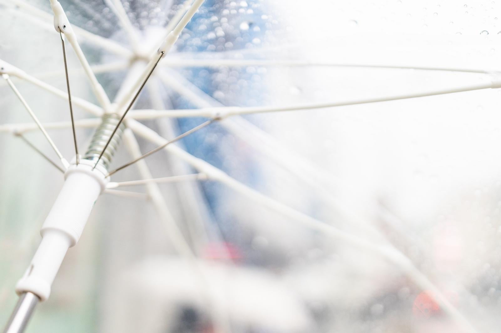 雨の中で差したビニール傘を内側から見上げた骨組みと水滴のアップ