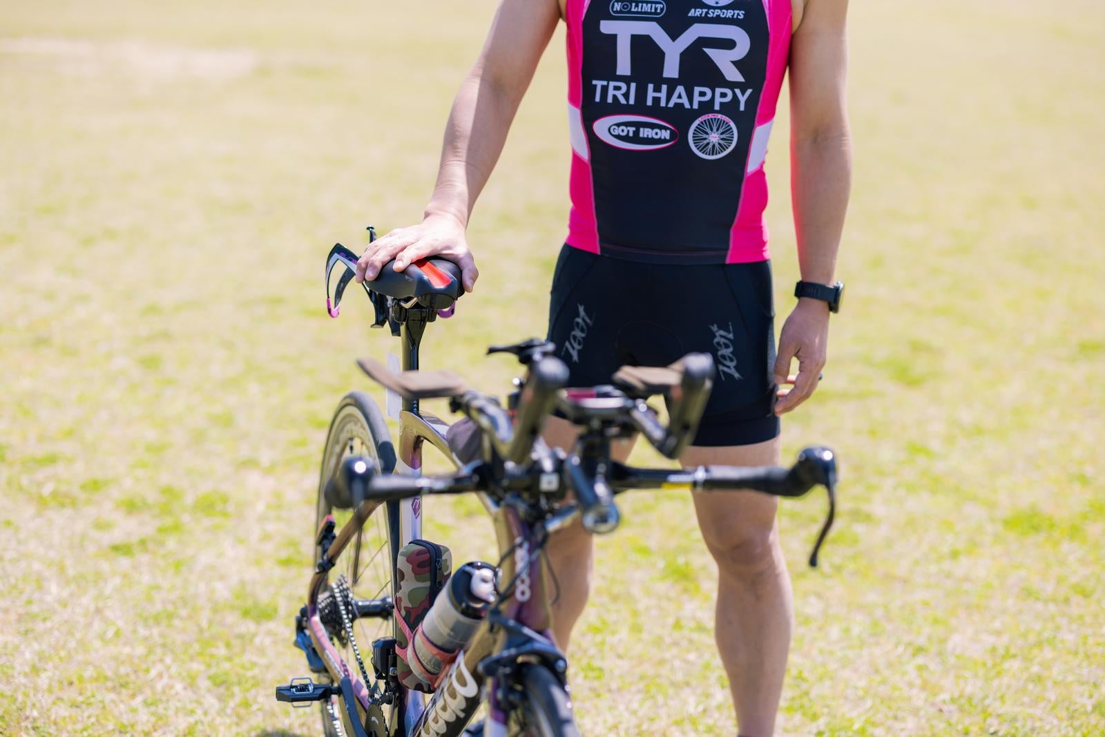 ロードバイクのサドルに手を添えて芝生に立つトライアスロンウェアの選手［モデル：うえせい］