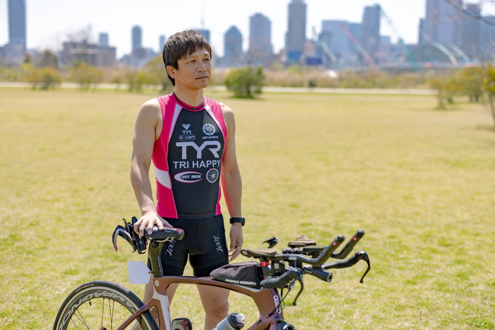 ロードバイクの横に立つトライアスロンウェア姿の男性サイクリスト［モデル：うえせい］