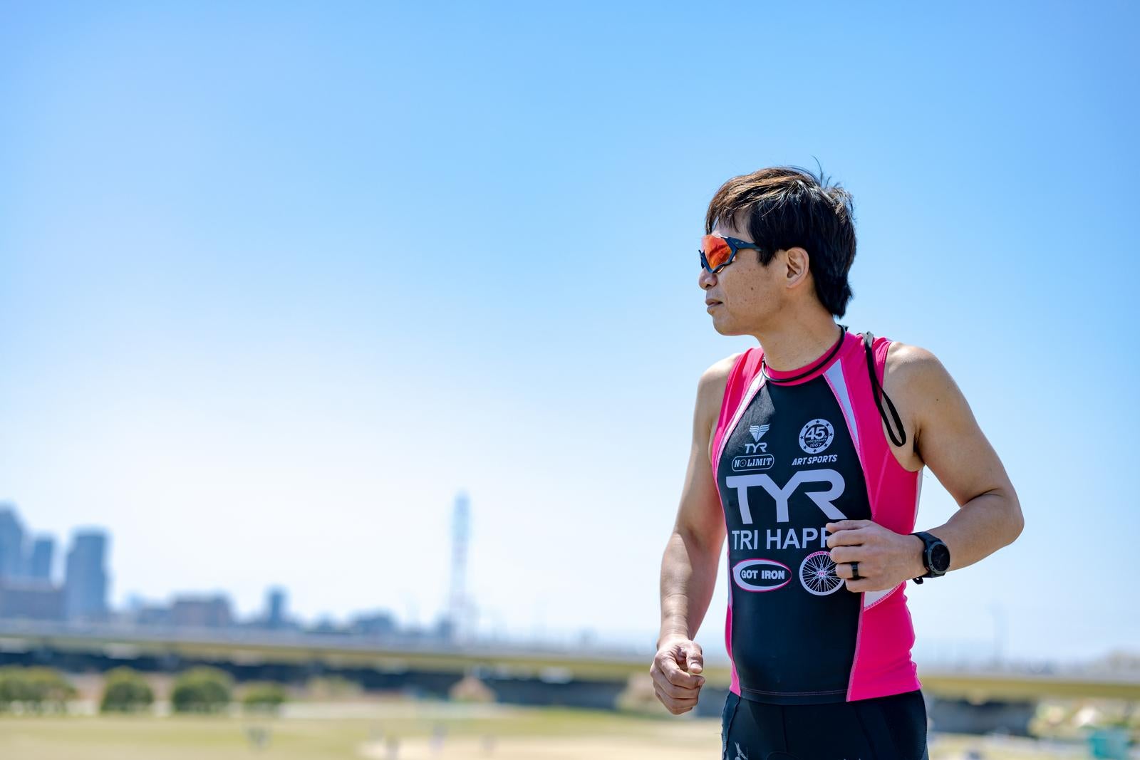 河川敷をジョギングするサングラスをかけたトライアスロン選手の男性［モデル：うえせい］