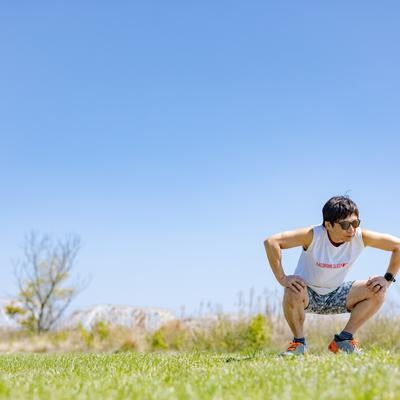 青空の下で屈伸する男性ランナーの写真