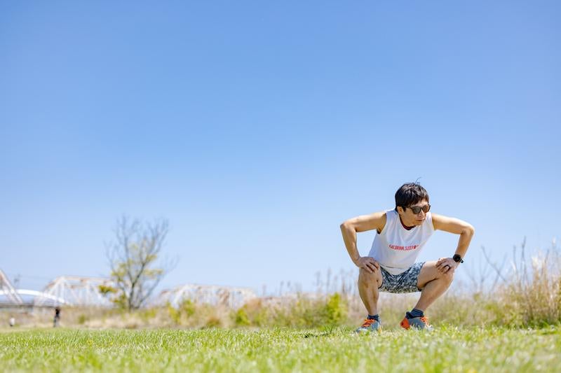 青空の下で屈伸する男性ランナーの写真