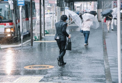 大雨と強風の中、出社する社畜ビジネスマン（びしょ濡れ）の写真