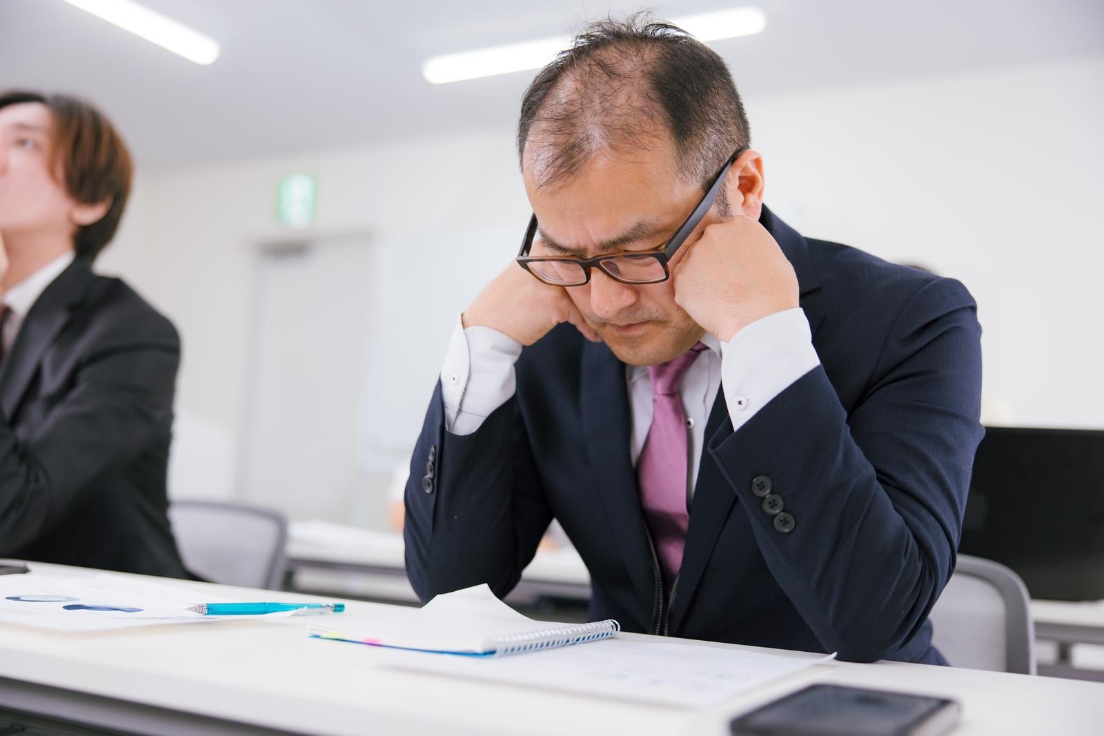 「会議中に疲労感で居眠りそうな管理職の男性」の写真［モデル：高木桂一］