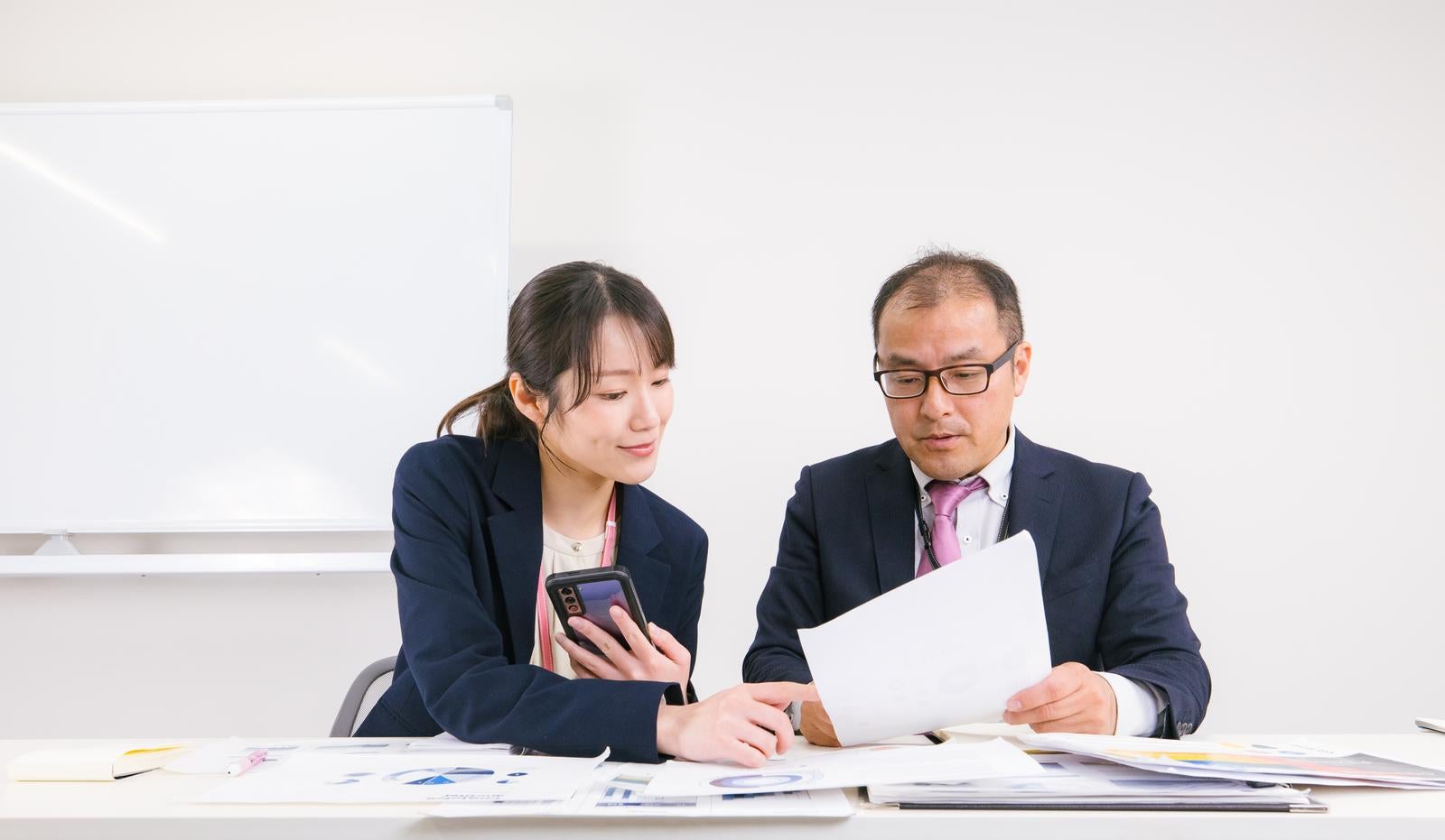 「ホワイトボード前で熱心に向き合うビジネスパートナー」の写真［モデル：高木桂一 SAKI］