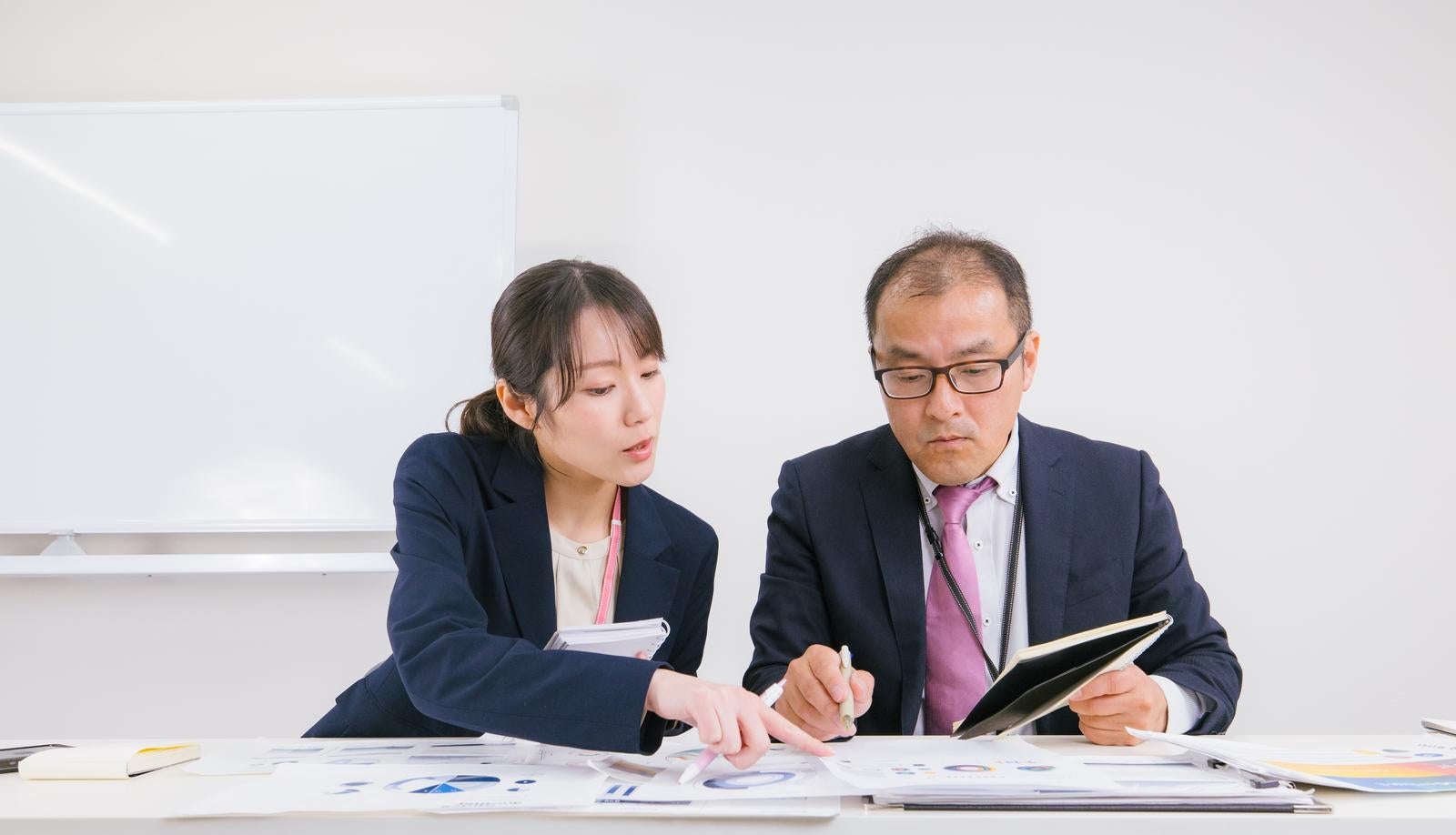 「会議室で書類を確認する男女の会社員」の写真［モデル：高木桂一 SAKI］