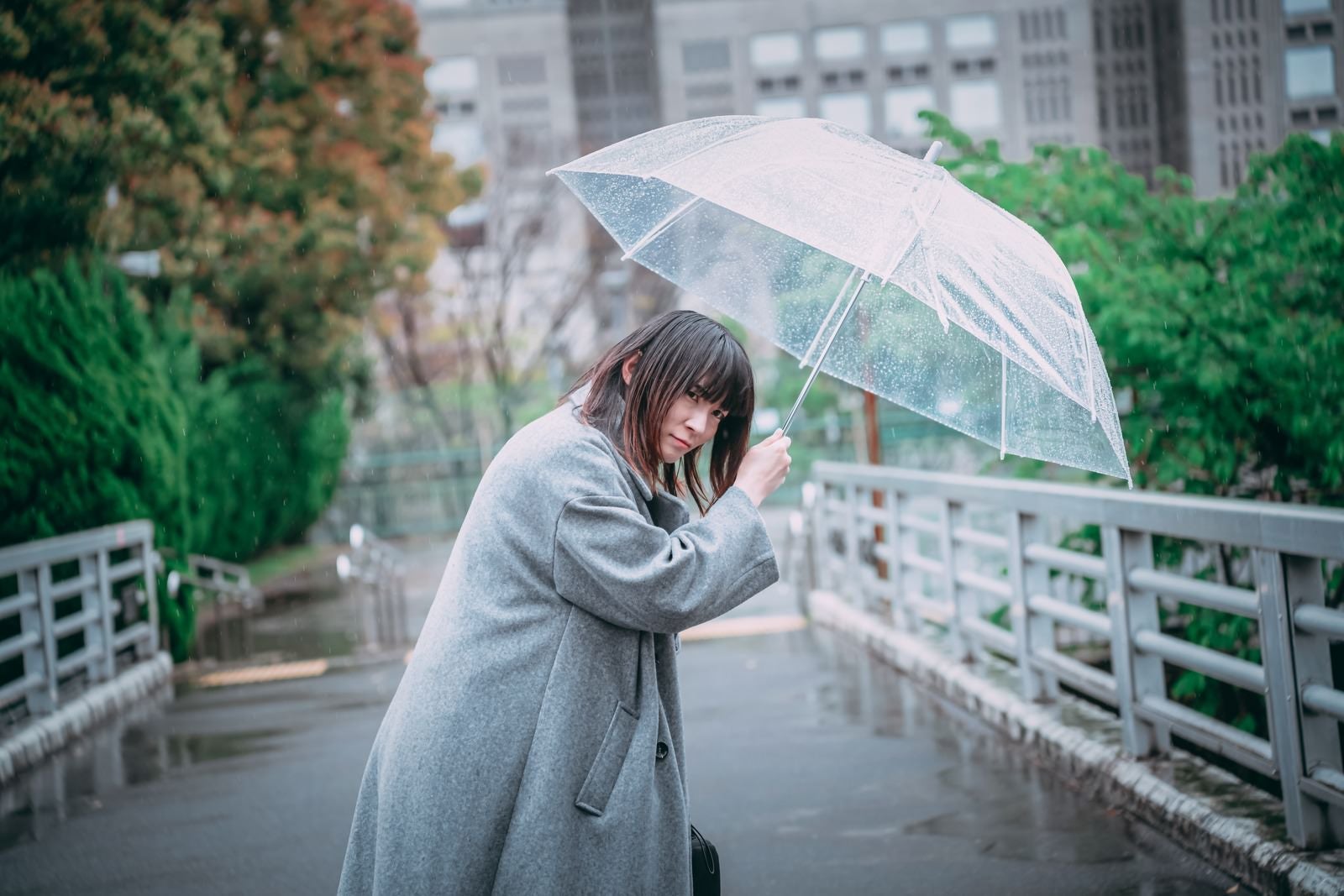 「ビニール傘を差して辺りを警戒する女性」の写真［モデル：たけべともこ］