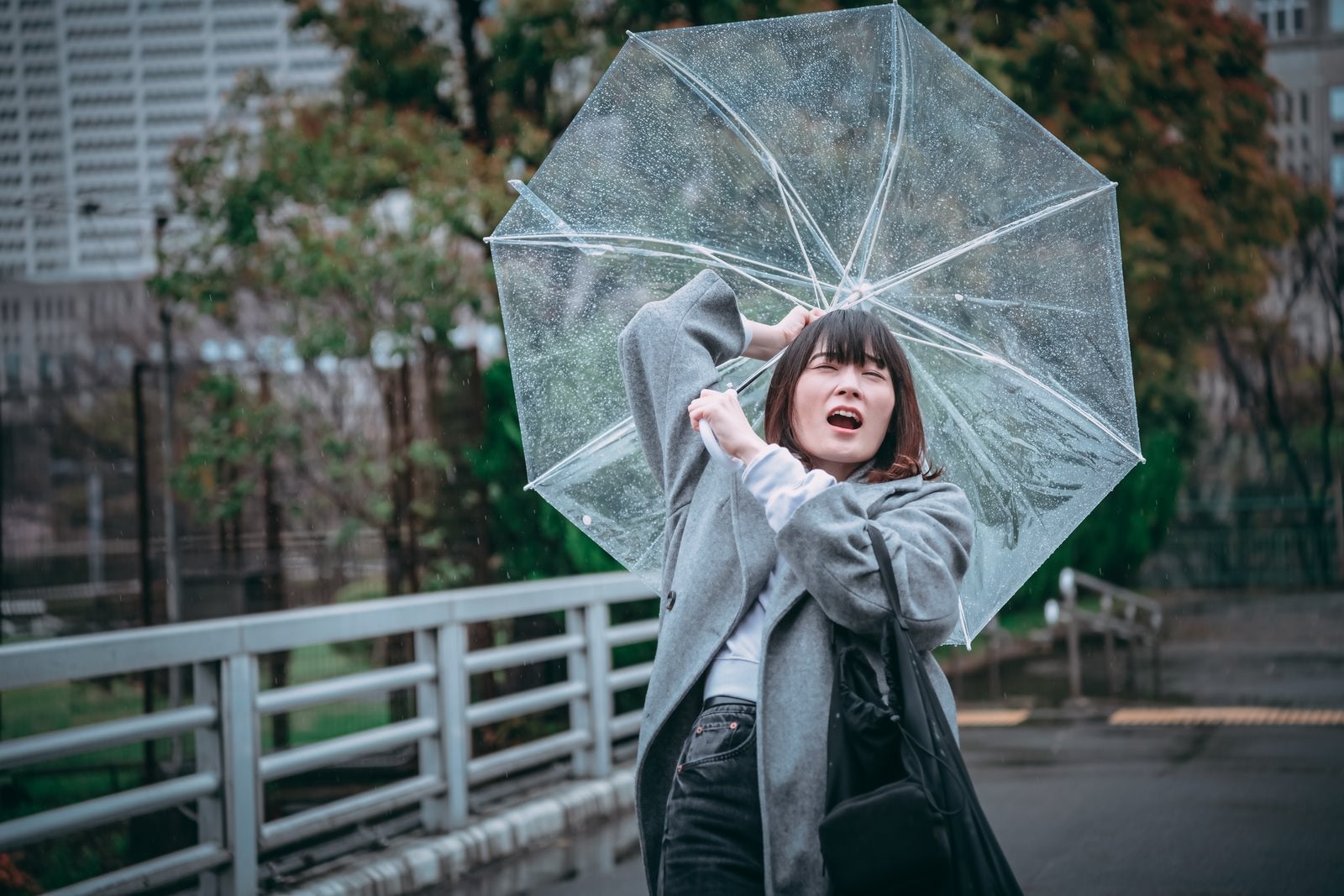 「風に飛ばされそうな傘を持つ女性」の写真［モデル：たけべともこ］