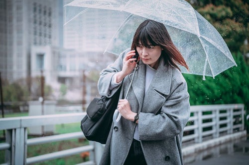 傘を差しながら通話する女性の写真
