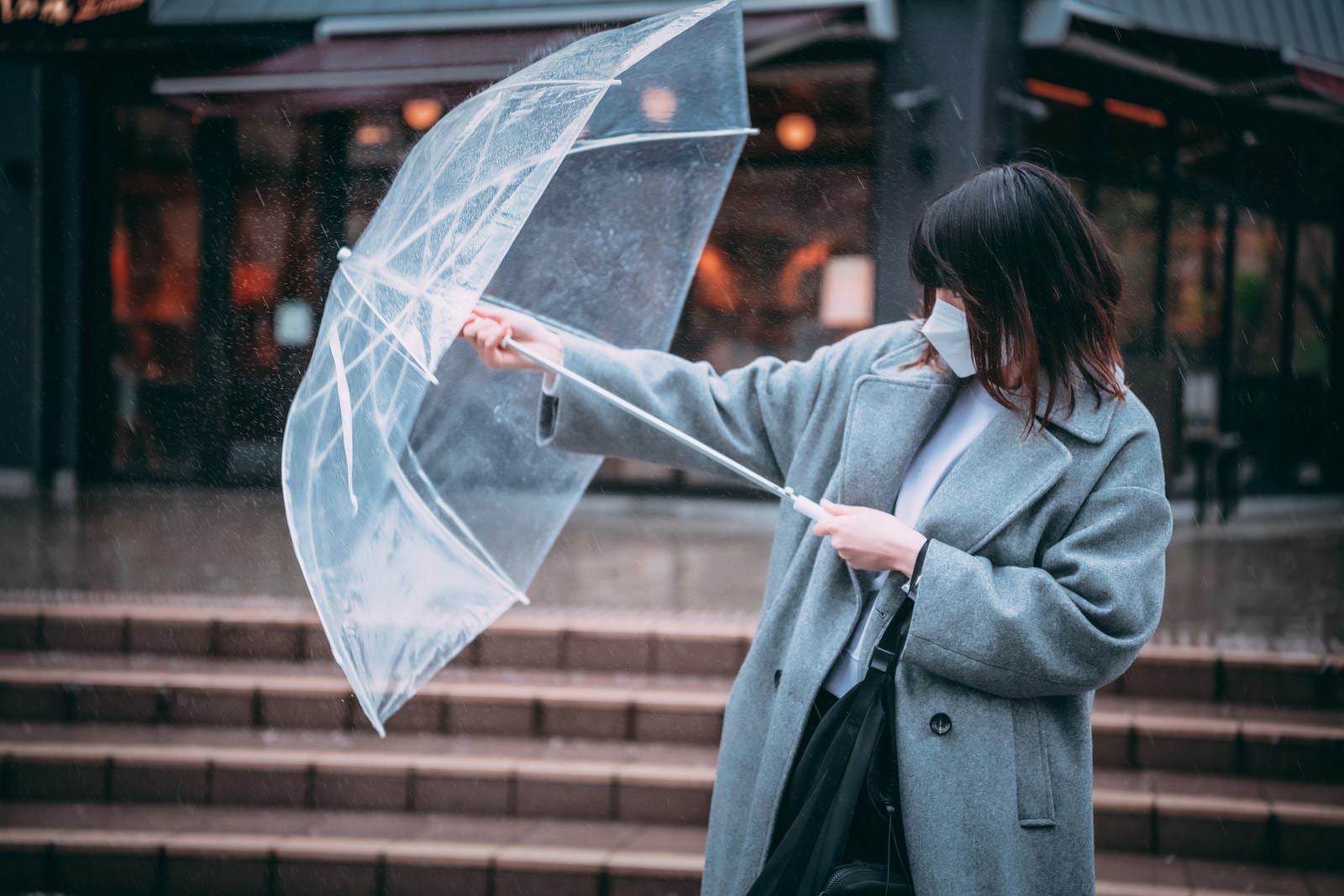 「前方からの雨にビニール傘で立ち向かう女性」の写真［モデル：たけべともこ］