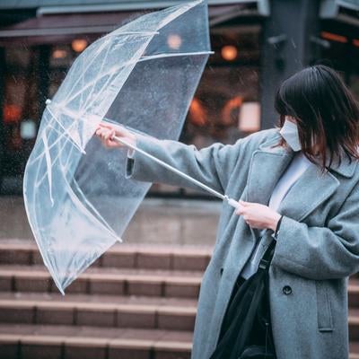 前方からの雨にビニール傘で立ち向かう女性の写真