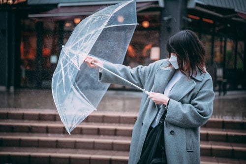 前方からの雨にビニール傘で立ち向かう女性の写真