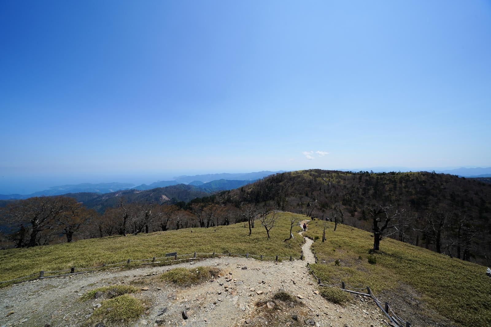 「登山道の先に広がる稜線と遠くに見える青い海」の写真