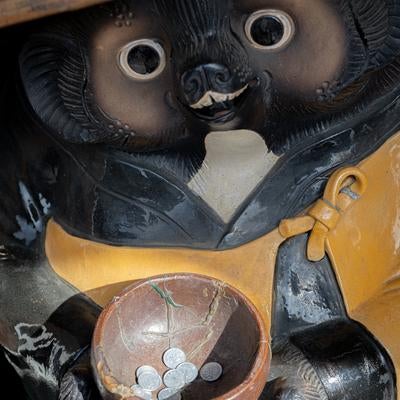 黄色い前掛けを着た狸の置物が腹に託鉢の鉢を抱える縁起物の写真