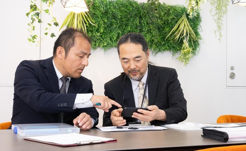スマホに送られてきたデータを紙で確認する管理職の写真