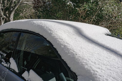 フロントガラスまで雪に覆われた乗用車の写真