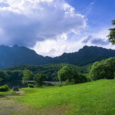 鏡池横に広がる草地と妙高戸隠連山国立公園の碑と奥にそびえる急峻な山の姿の写真