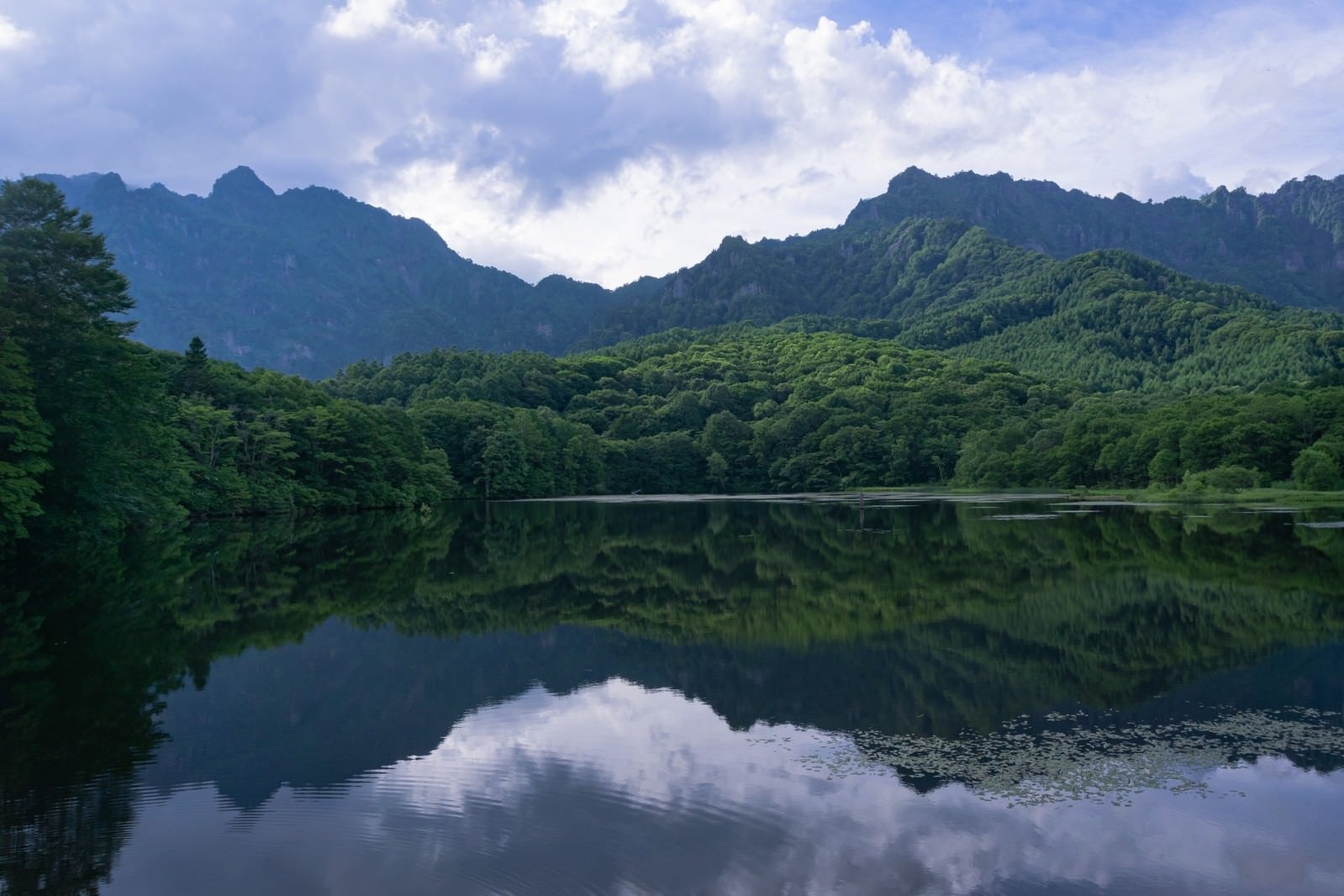 「緑豊かな木々と険しい神話の山を映す夏の鏡池」の写真