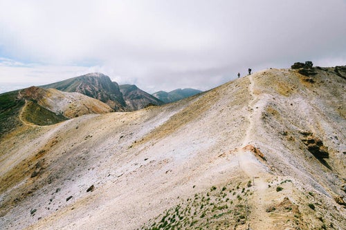 雲が広がる稜線を歩く登山者の写真
