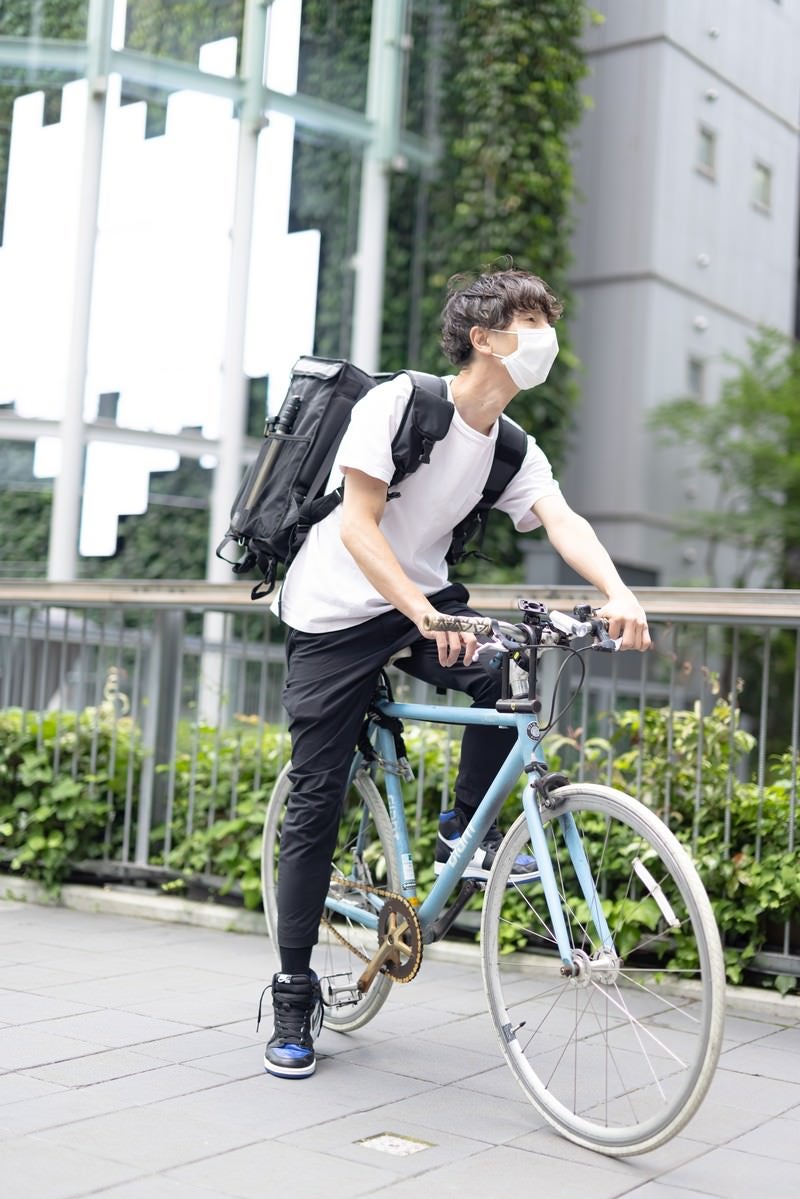 「自転車に乗って配達する男性」の写真［モデル：TSURUTAMA］