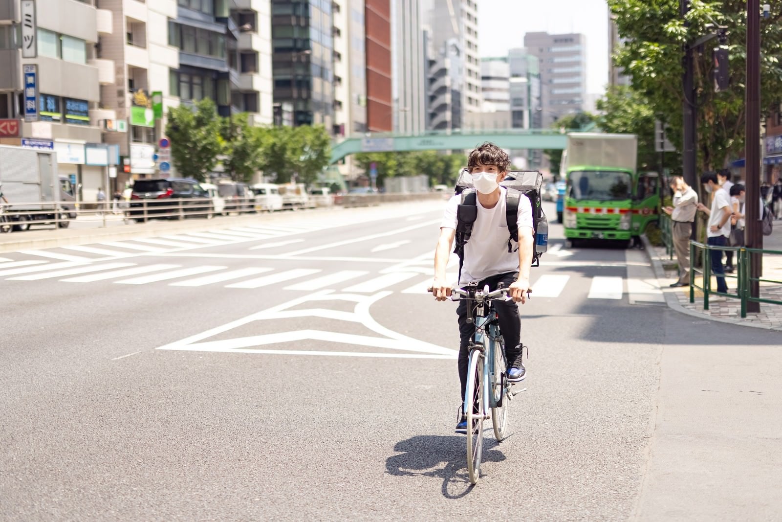 「自転車に乗って配達場所に向かうフードデリバリーの男性」の写真［モデル：TSURUTAMA］