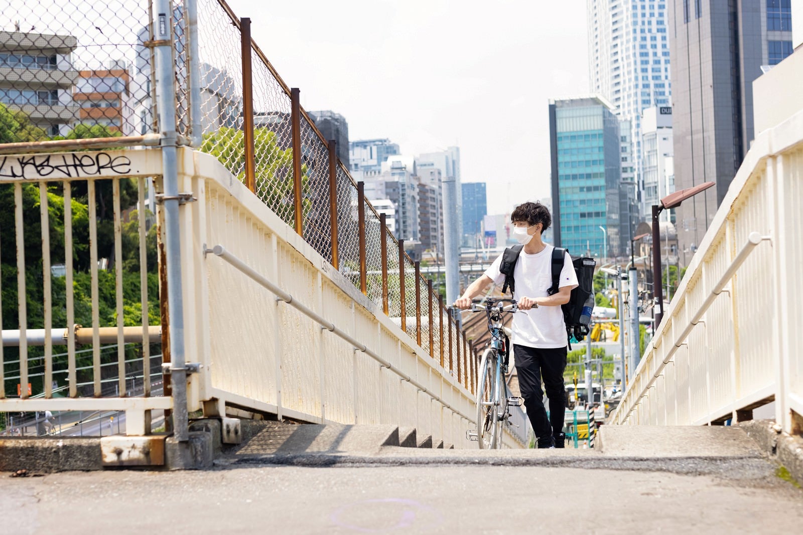 「歩道橋の階段を歩くフードデリバリーの男性」の写真［モデル：TSURUTAMA］