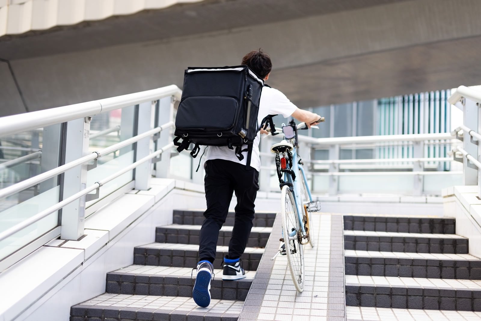 「自転車を押して歩く配達員」の写真［モデル：TSURUTAMA］