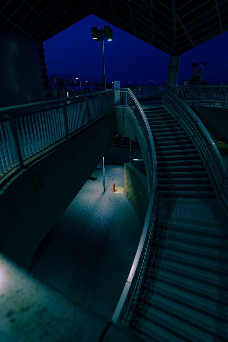 深夜の歩道橋にひとつだけ残されたコーンの写真