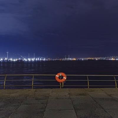 オレンジ色の救命浮環と対岸の工業地帯夜景の写真