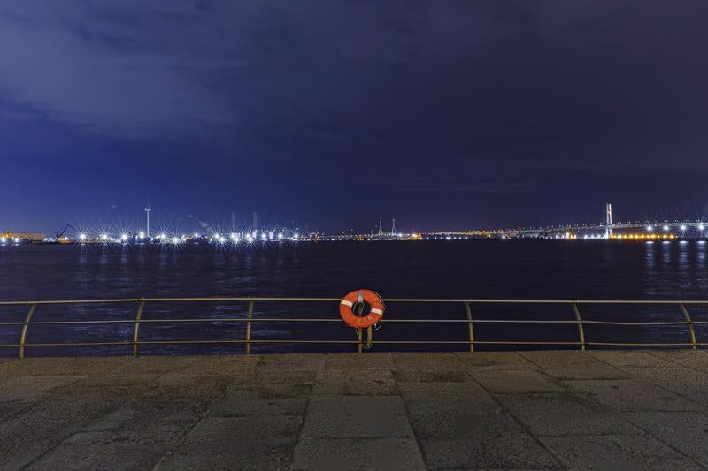 オレンジ色の救命浮環と対岸の工業地帯夜景の写真