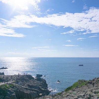 日の光に輝く海と東尋坊の崖上の観光客の写真
