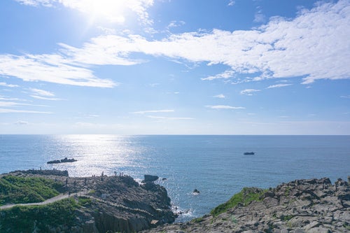 日の光に輝く海と東尋坊の崖上の観光客の写真