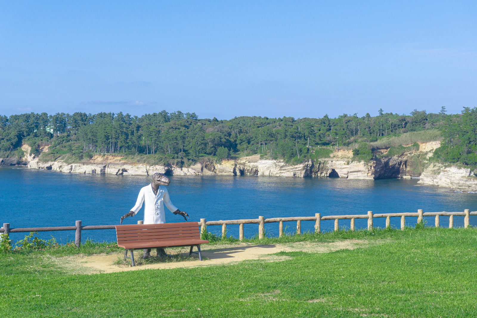 「東尋坊北の芝生広場に配置された恐竜博士ベンチと福良の浜の海食崖と海食洞」の写真