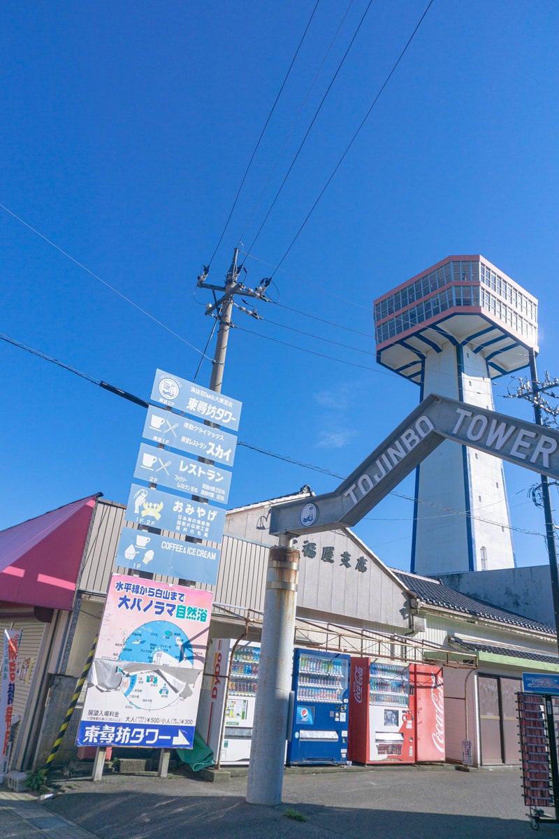 青空の下にそびえる白い東尋坊タワーと手前に設置された複数の案内看板