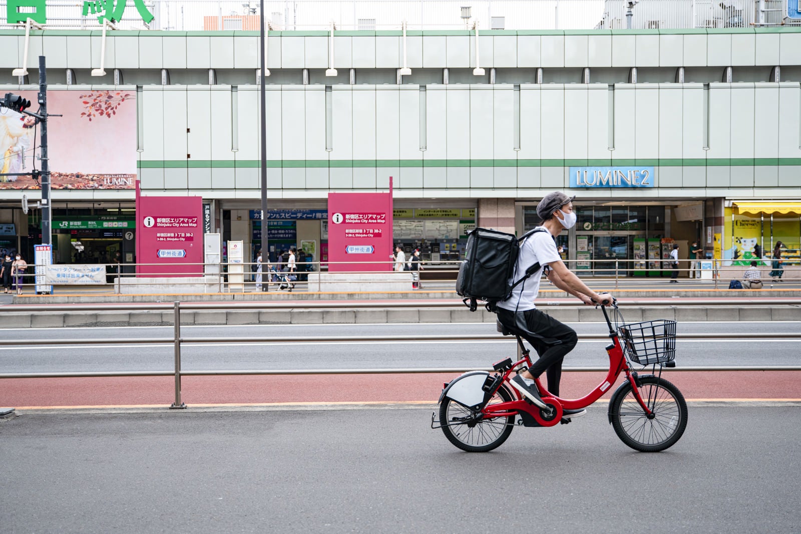 「新宿駅前を走行するフードデリバリーの配達員」の写真