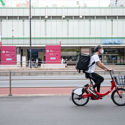 新宿駅前を走行するフードデリバリーの配達員の写真