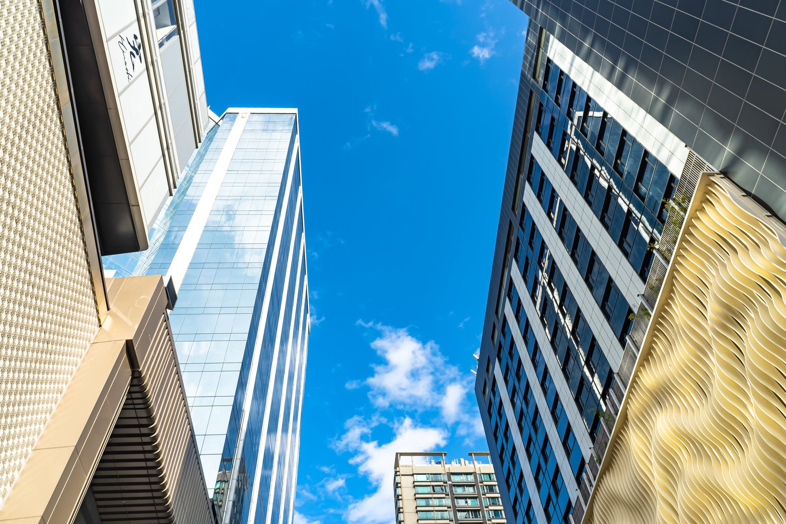 香港の高層ビル群を真下から見上げた青空とガラス張りのビル