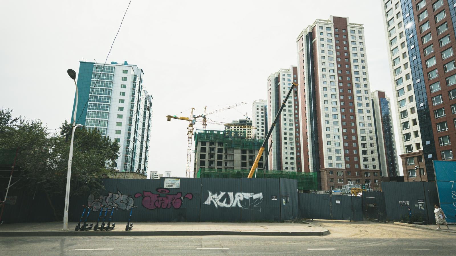 グラフィティが描かれた仮囲いの向こうにクレーンと高層ビルが立ち並ぶウランバートルの街並み