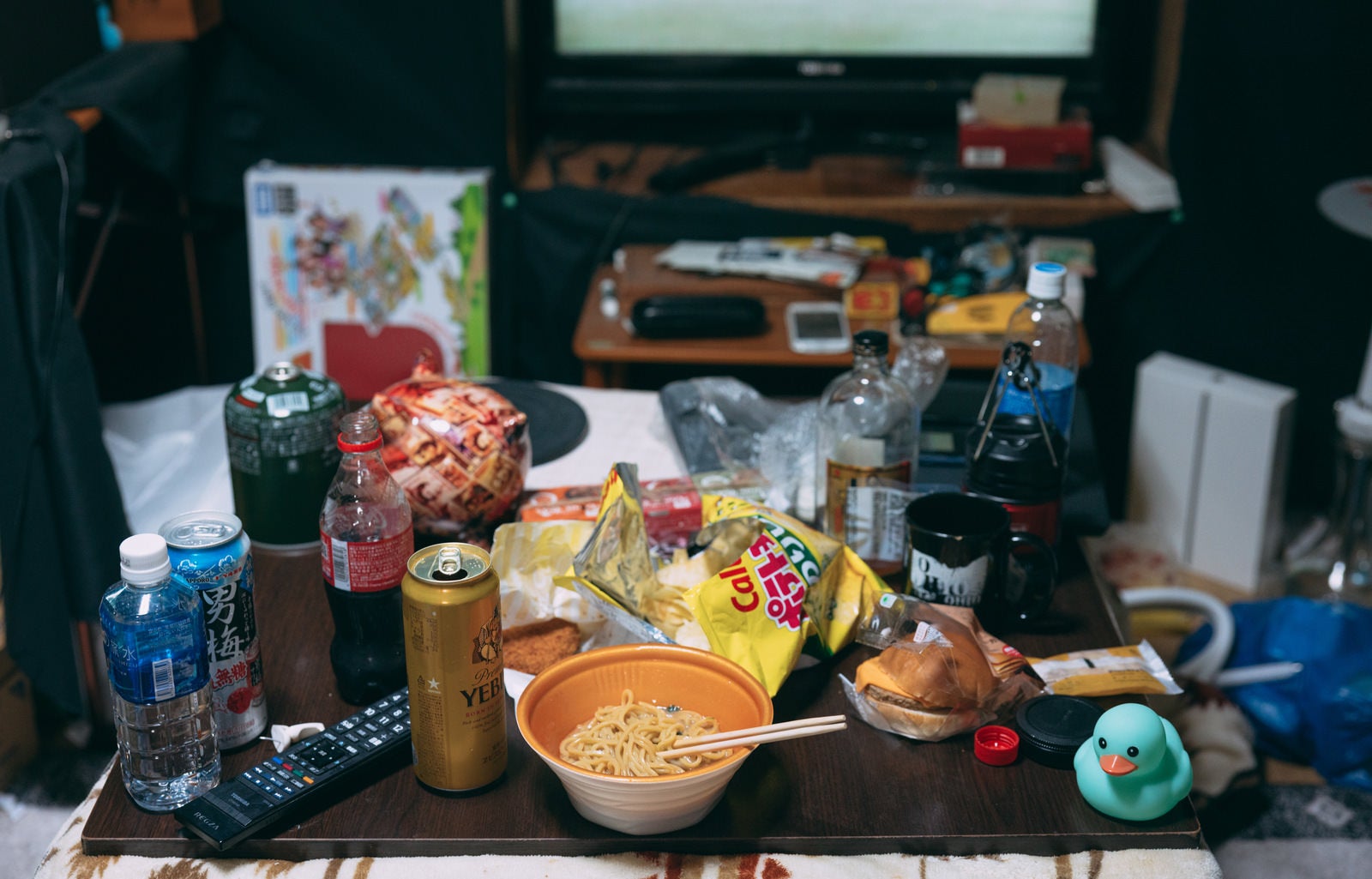 焼きそばの丼やビール缶、スナック菓子の袋がテーブルに散乱する汚部屋