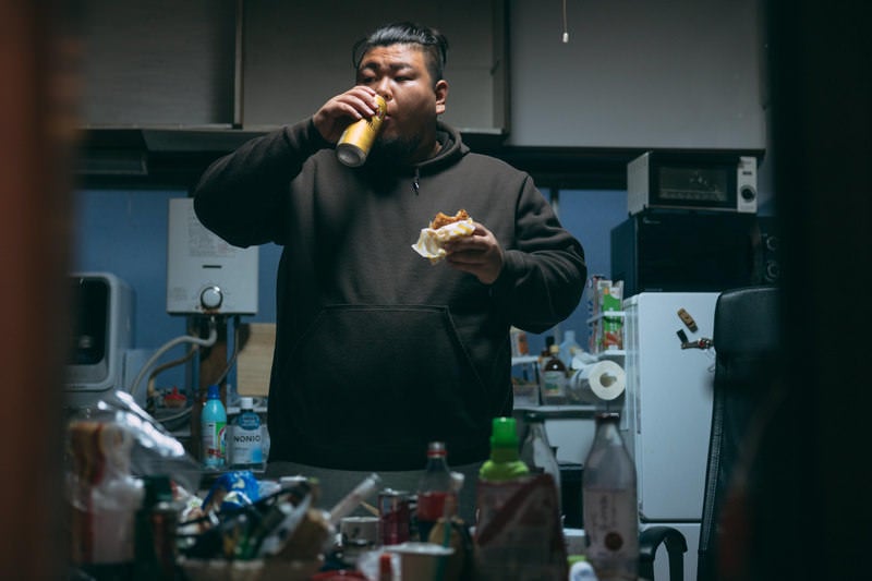 散らかったキッチンで立ち飲みする男性の写真