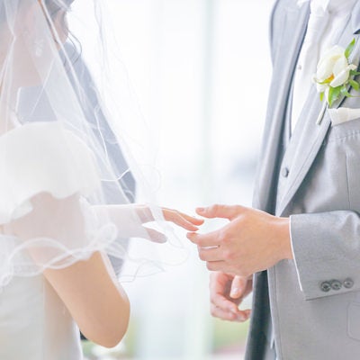 花嫁の左手を持って指輪をつけようとする新郎（ウエディング）の写真