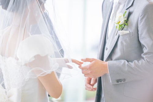 花嫁の左手を持って指輪をつけようとする新郎（ウエディング）の写真