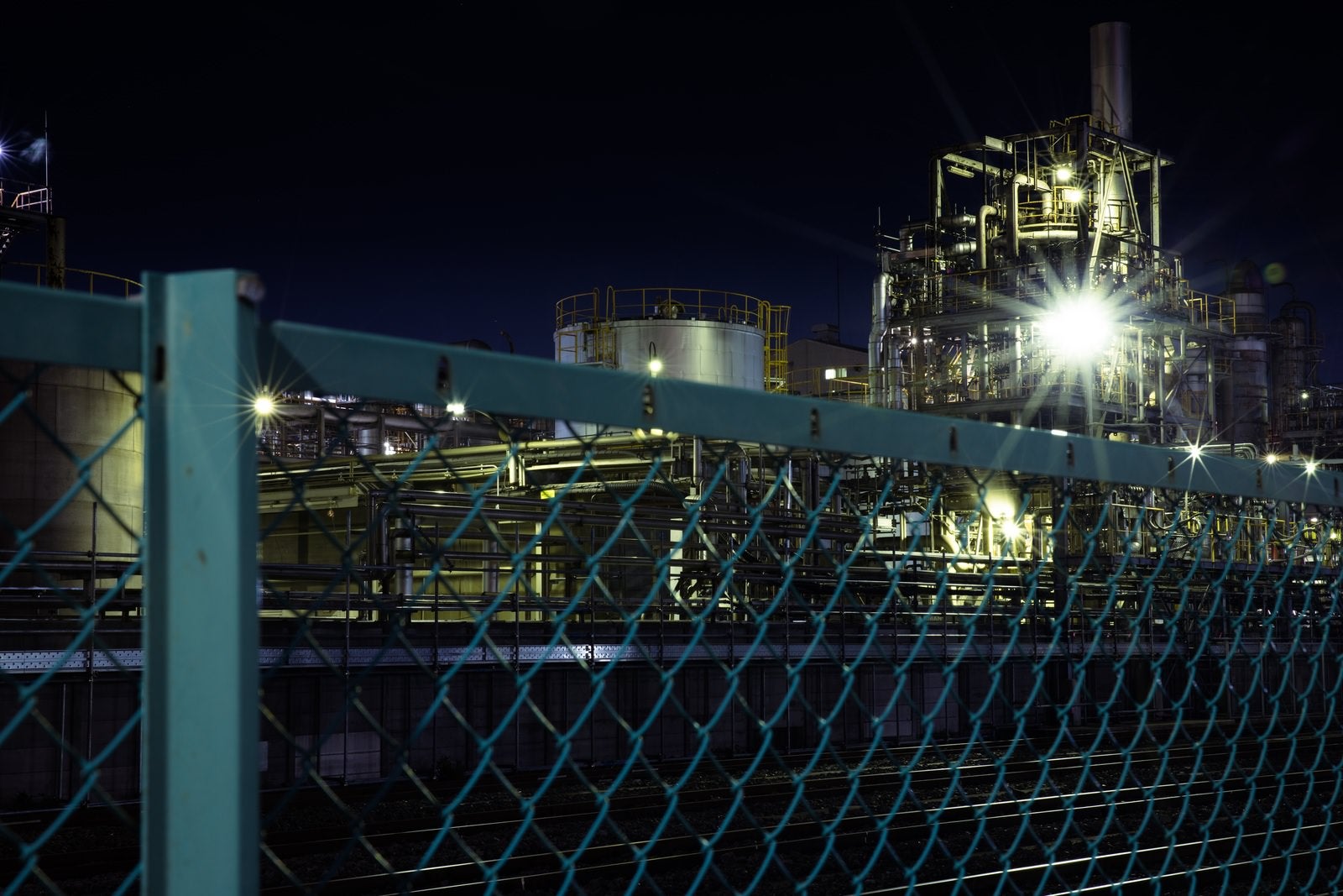 「フェンス越しの工場夜景と光芒」の写真